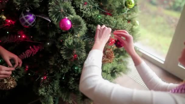 光沢のあるボールやおもちゃで自宅でクリスマスツリーを飾る2人の女性のクローズアップ 多色の花輪で点滅する木 ビデオ — ストック動画