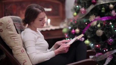 Kafkas kadının Noel ağacı ve şömine ve okuma kitabı yakınında koltukta oturan video 