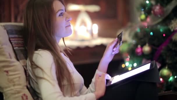 여성이 크리스마스 근처의 의자에 카드로 온라인 쇼핑을하는 디지털 태블릿을 사용하는 — 비디오