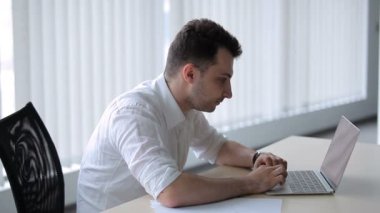 Genç adam ofisteki masada oturur. Adam videoyu izliyor ve sevinmek için yalvarıyor..