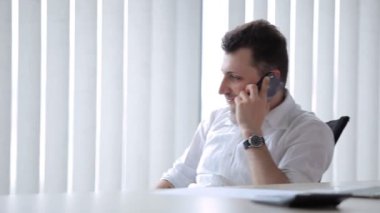 Genç adam sandalyeye oturur. Adam elinde kalemle sandalyede döner, telefonda duygularıyla konuşur..