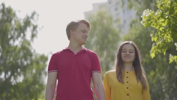 緑の春の公園で歩く愛の幸せな白人のカップル。若い美しい男女の日付。屋外でロマンチックな時間を過ごす. — ストック動画