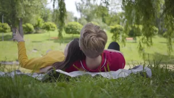 Joven pareja feliz en el amor haciendo picnic acostados juntos en el hermoso jardín floreciente o parque relajante y sonriente — Vídeos de Stock