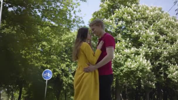 Tierna pareja caucásica enamorada tiernamente abrazándose y sonriendo en el fondo del verde parque de primavera. Fecha de joven hermoso hombre y mujer. Romántico pasar tiempo al aire libre . — Vídeos de Stock