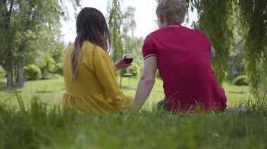 Aşık genç mutlu çift güzel çiçeklenme bahçe veya parkta neşeyle sohbet ve gülümseyerek şarap ile piknik yapma. Genç güzel erkek ve kadının tarihi. Romantik vakit geçirmek dışarıda.