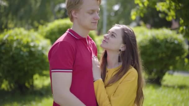 Feliz pareja caucásica enamorada tiernamente abrazándose y sonriendo en el fondo del verde parque de primavera. Romántico pasar tiempo al aire libre. Movimiento lento . — Vídeo de stock