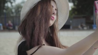 Yaz beyaz şapkalı sevimli genç kadın sahilde dinlenen cep telefonuyla selfie çekiyor. Yaz eğlence konsepti. Hafta sonu saati