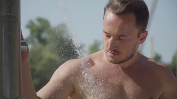 屋外のビーチシャワーで水の下で洗う強い男クローズアップ。夏のレジャー。ボディケア — ストック動画