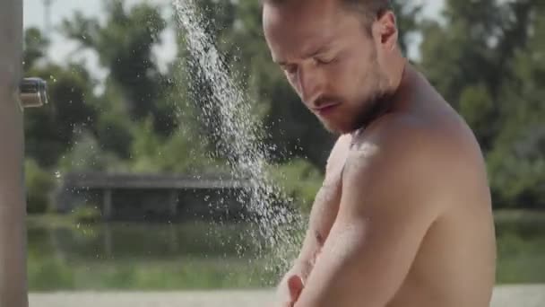 屋外のビーチシャワーで水の下で洗う魅力的な運動男クローズアップ。夏のレジャー。ボディケア — ストック動画