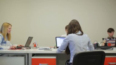 Ofis masalarında çalışan beş genç erkek (üç erkek ve iki kız).