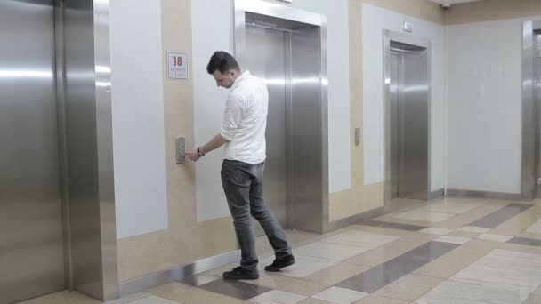 人走到电梯前 按下按钮 这个按钮坏了 那家伙看了看表 按了一下电梯按钮 那家伙又按了一个按钮 但没有用 那家伙把他的手撞到墙上 怒气冲冲地离开了 — 图库视频影像