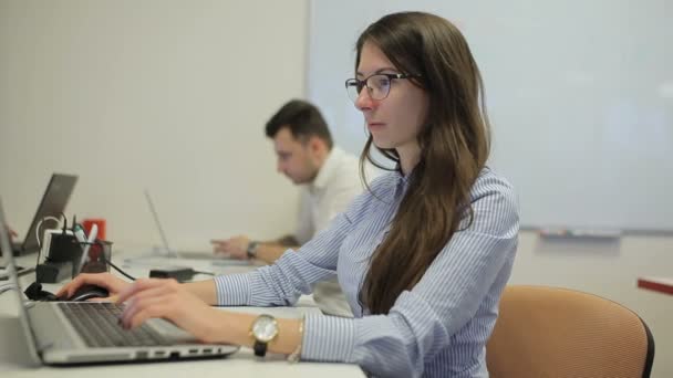 オフィスのノートパソコンにタイプするメガネの若い女性 キーボードを入力している若い男性の背景に — ストック動画
