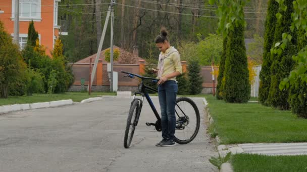 路上で自転車を持ちながら携帯電話でタイプする若い女の子のビデオ 男が乗って — ストック動画