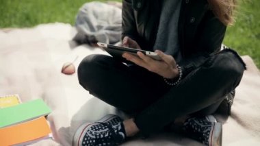 Büyüleyici kız öğrenci kampüste bir tablet kullanarak açık havada öğrenme. Yeşil çimenler üzerinde battaniye üzerinde çapraz bacaklı ile oturan öğrenci, video