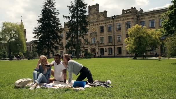 大学の外の芝生の上に毛布の上に座って 自分自身の写真を撮る学生のグループ ビデオ — ストック動画