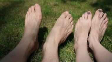 Erkek ve dişi ayaklar çimlerin üzerinde. Adam ayak parmaklarını oynatıyor ve kızın ayaklarına dokunuyor..
