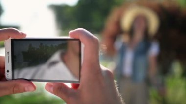 Adam akıllı telefonu elinde tutuyordu. Adam telefonda kızın fotoğrafını çekti. Gülümseyen ve poz veren kız.
