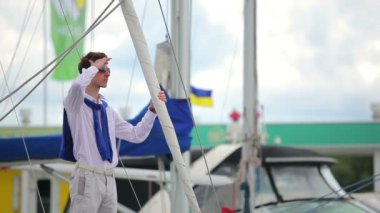 Adam seni bekliyor. Adam elini alnına koyar ve uzaklığa bakar. Adam adamı görür ve mutlu bir şekilde el sallar. Adam el sallıyor ve birini davet ediyor. Gülümseyen ve el sallayan adam.