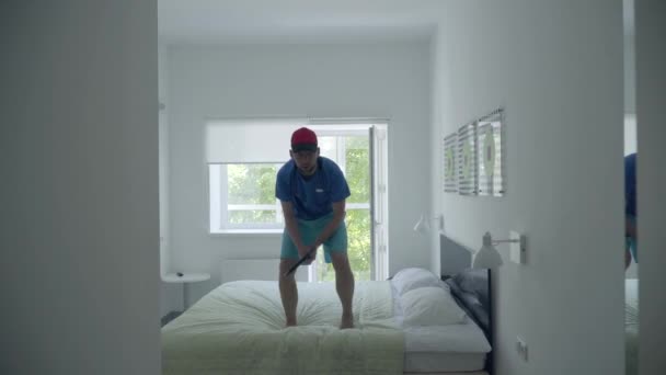 Hombre joven entrenando para jugar al tenis de pie en la cama en la cómoda habitación del hotel. Estilo de vida activo. Cámara acercándose — Vídeos de Stock