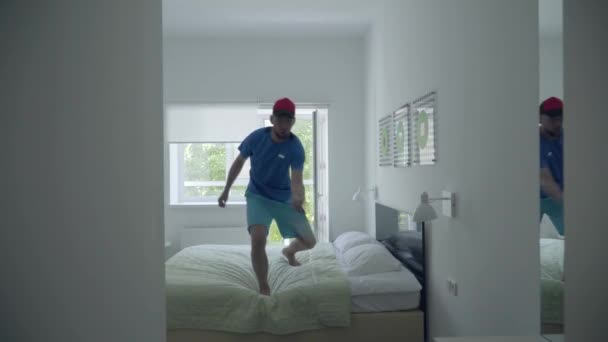 Hombre joven entrenando para jugar al tenis de pie en la cama en la cómoda habitación del hotel. Estilo de vida activo. Deportes y recreación . — Vídeos de Stock