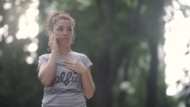卷曲的女孩在智能手机上说话 而站在公园 看着相机微笑 — 图库视频影像