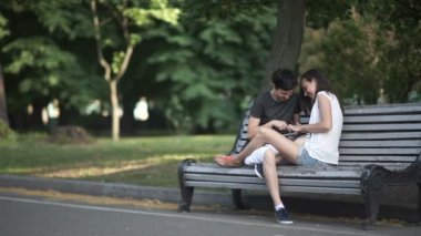 İki güzel lezbiyen bir parkta bankta oturan, gülerek ve dijital tablet kullanarak 