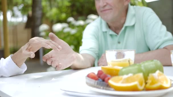 テーブルで庭に座っている間に手をつないでいる高齢のカップル ビデオ — ストック動画