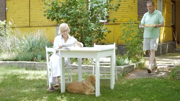 Eine Ältere Frau Sitzt Tisch Hof Mann Bringt Tablett Mit — Stockvideo