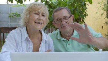 Yaşlı çift dizüstü bilgisayarda web kamerasında ellerini sallıyor. Bahçede dizüstü bilgisayarla konuşan yaşlı bir çift. Bahçede dizüstü bilgisayarı olan yaşlı bir çift. Yakın plan..