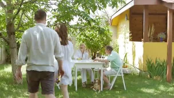 年轻人送给一对老夫妇礼物 一个年轻的家庭花时间与妻子的父母在一起 人们在花园里的小木屋里玩得很开心 — 图库视频影像