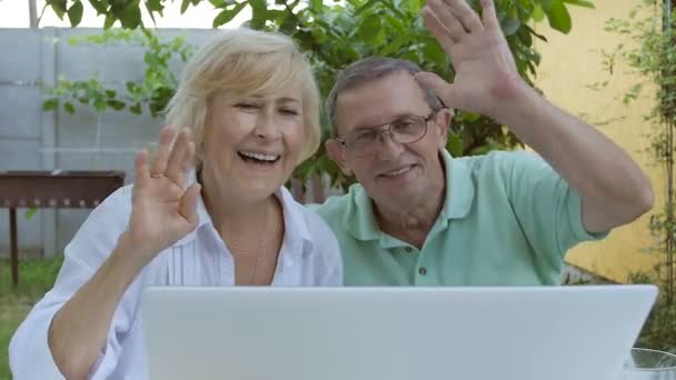 ラップトップのウェブカメラで話している高齢者のカップル 老夫婦はノートパソコンのウェブカメラで手を振っていた 庭にノートパソコンを持って座っている老夫婦 — ストック動画