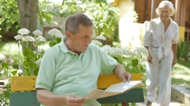 Olgun bir eş, kürsüde oturan kocasına gelir. Erkek ve kadın bahçede oturuyor ve gülümsüyor. Yaşlı bir adam bahçede bir bankta oturur ve bir gazete okur..