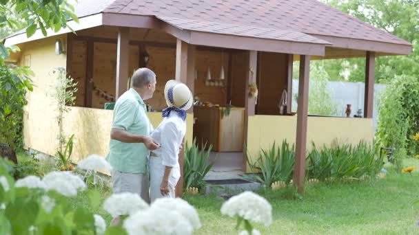 老人と女性は鍵を手に持っている 庭の家の近くに老夫婦が立っている 女と男が抱き合っていた 親指を立てた年配の女性が — ストック動画