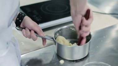 Aşçı hamuru tavaya yoğurur. Adamın biri plastik kürek kullanıyor. Masanın yanında elektrik var. Bir fırıncının restoranın mutfağında hamuru yoğurması gibi kamera da yakın plan çekiyor. Kışkırtıcı bıçağın içinde bulunduğu tencerelere yakın çekim.