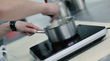 Aşçı hızla tavanın içindekileri karıştırır. Pan elektrikli sobanın üzerinde duruyor. Tencereden buhar fışkırıyor. Aşçı tencereyi kaldırıp sallıyor. Adam tavayı elektrikli ocağa koyuyor. Aşçı hamuru tavada yoğurur..