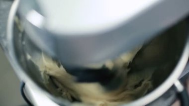Birleştir. Hamur artık karıştırılmıyor. Cook kaseyi kışkırtıcıyla alıyor. Kışkırtıcı hamuru bir kasede karıştırmaya başlar. İnsan işlemciyi de içerir. Kamera ortalığı karıştırmanın büyük bir getirisi. Yakın plan..