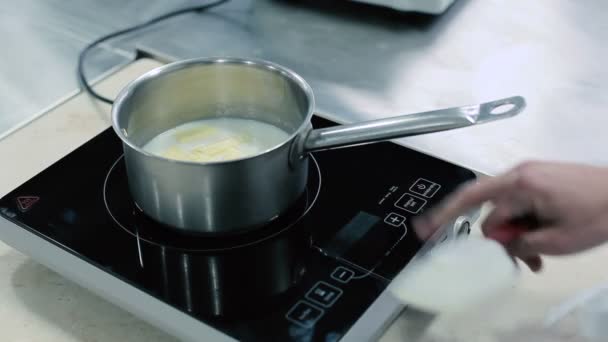 牛乳とバターを鍋で加熱する 鍋の内容のクローズアップ 調理混合へらバターミルク パンはテーブルの上の台所の電気ストーブです 表示をクリックし 電気ストーブの加熱を制御します — ストック動画