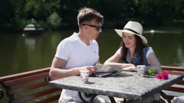 Genç bir çift nehir kenarındaki haritaya bakıyor. Adam kız arkadaşına nereye gideceğini gösterir. Kız ellerini çırpıyor, tatmin oluyor ve erkek arkadaşının yanağından öpüyor. Çift gülüyor..