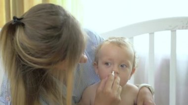 Anne, kızının burnuna sprey sıkar. Yakın plan. Bebek burnunu kaşıyordu. Annem tacın içindeki kızı öpüyor. Küçük bir kıza sarılan kız.