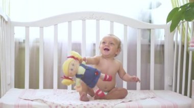 Oyuncak bebek tutan küçük bir kız. Oyuncak bebek annesine veriyor. Bebek karyolada oturuyor ve gülüyor. Bebek karyolasında oturan küçük kız. Bebek yana bakıyor..