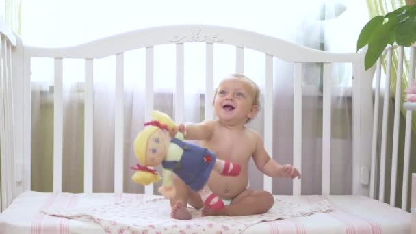 抱着玩具娃娃的小女孩 娃娃给了她妈妈 婴儿坐在婴儿床上笑着 小女孩坐在一个婴儿床里 婴儿把目光移开 — 图库视频影像