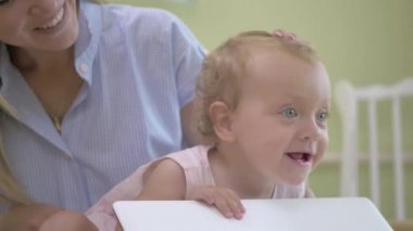 Bebek dizüstü bilgisayarın kapağını hareket ettiriyor. Anne ve bebek kameraya el sallıyor. Anne ve bebek beyaz bir dizüstü bilgisayarın yanında bir yatakta oturuyor. Pembe elbiseli bir bebek ve başı için bandaj..