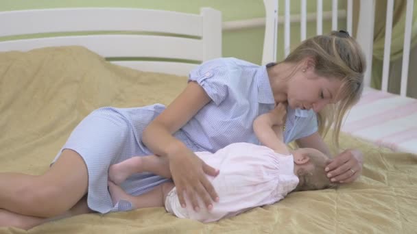 幼い娘を母乳で育てる母親 女は赤ん坊を母乳で育て始める 赤ん坊は母親の横に横たわってミルクを飲む ピンクのドレスを着た赤ん坊と頭のための包帯 — ストック動画