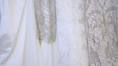 Yakın çekim, yavaş çekim. Kamera yavaşça aşağıdan yukarıya hareket eder. Kamera lüks dekorasyonu ve küçük unsurları olan güzel gelinliklere odaklanıyor. Gelinlikler düğün butiğindeki askılarda asılı..
