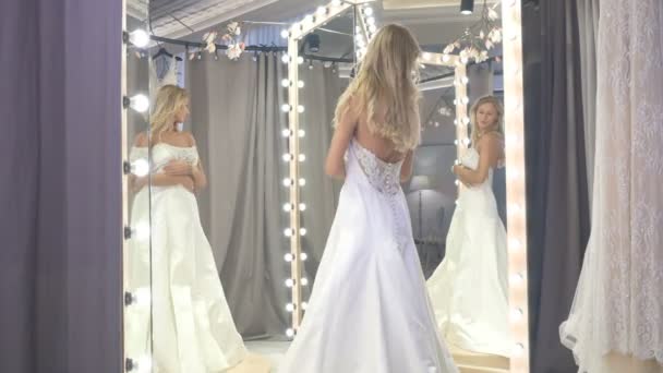 漂亮的新娘穿着白色豪华婚纱 呆在镜子前的婚纱精品店里 漂亮的姑娘穿上婚纱 从不同的侧面照镜子 — 图库视频影像