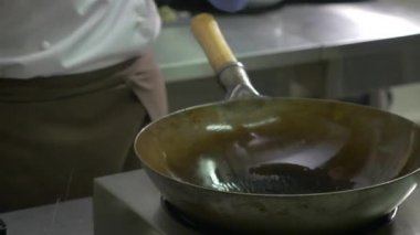 Yakın plan. Aşçı, yağlı sarı bir şişe alır ve onu sıcak bir tavaya döker. Adam sol eline bir tava alıp tavayı kepçeyle yağlamaya başlıyor. Adam fırının üzerinde daireler çizen bir tavayı hareket ettiriyor..