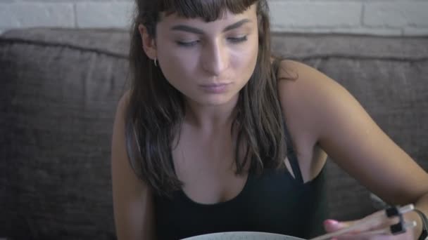 摄像机从上往下移动 它专注于一个盘与美味的菜肴 年轻的女人手里拿着筷子坐在桌子上 靠着盘子 吃着面条和蔬菜 — 图库视频影像