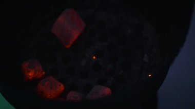 Close-up. The hookah touching the live coals with metallic forceps. The hookah turns the live coals and shakes them one after another in the iron bowl. Many red sparks falls on a sieve from live coals.
