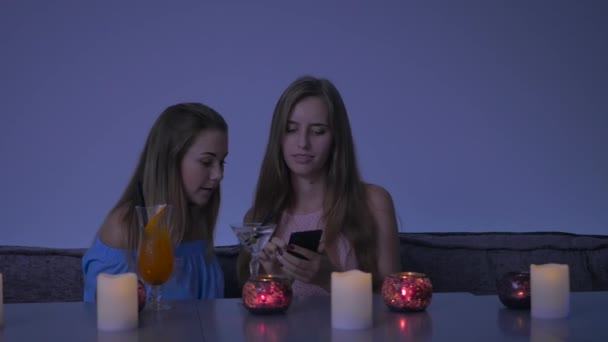 两个漂亮的女孩坐在咖啡厅里重拍 一个长头发的可爱女孩和她的朋友在智能手机上自私自利 这个女孩把电话给了她的朋友 然后给她的朋友拍了一张鸡尾酒照片 两个女孩在自作主张 — 图库视频影像