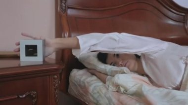 Genç esmer kadın yatakta uzanıyor, dinleniyor, çalar saate dokunuyor ve yatağın yanındaki masaya fırlatıyor. Çekici genç kadın yatağın diğer tarafına döner ve uyumaya devam eder..